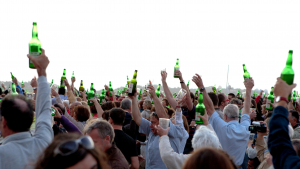 Personas levantando la botella de sidra para realizar el escanciado simultáneo en la playa de Poniente, Gijón