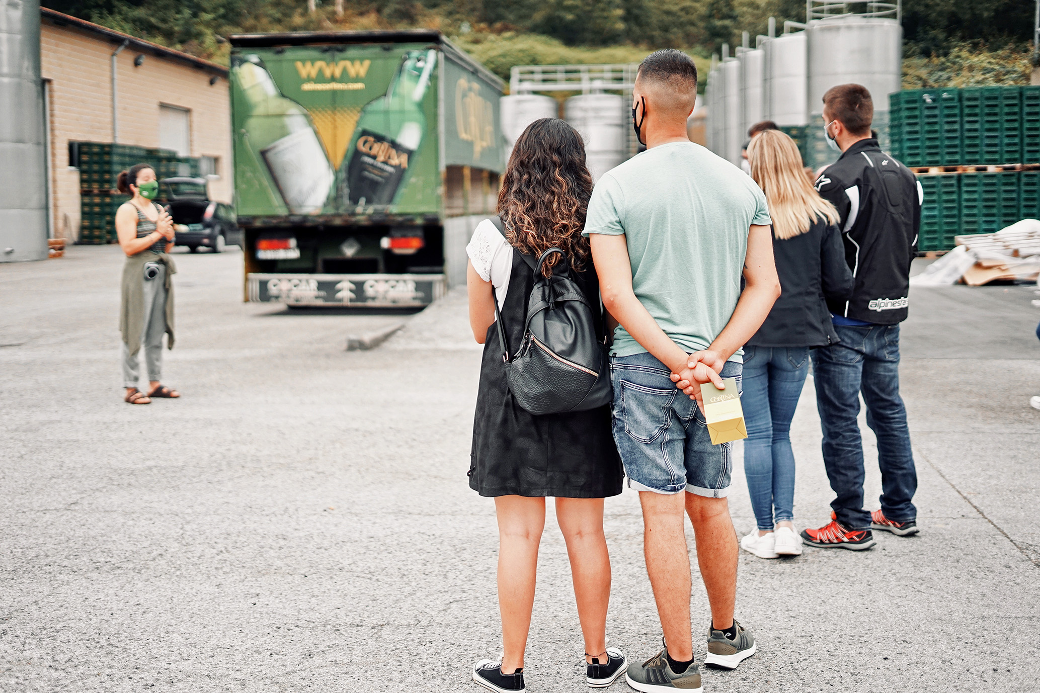 Personas de espalda realizando una visita guiada en las instalaciones del llagar de sidra Cortina, con un camión al fondo de la empresa