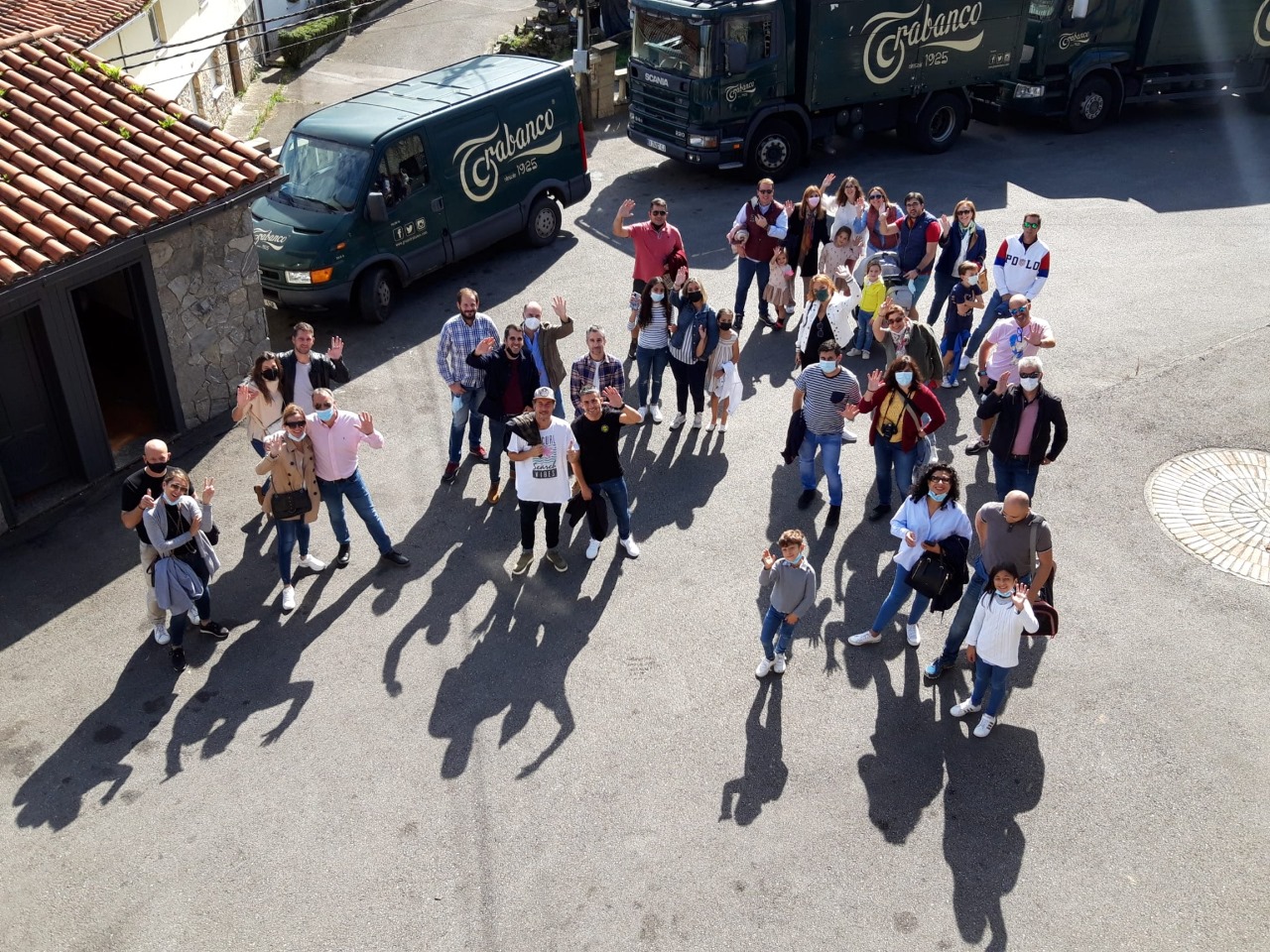 Personas saludando en la visita a las instalaciones de sidra Trabanco, en el exterior con camiones de la empresa detrás