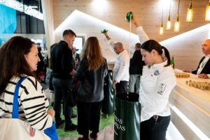 Personas escanciando en zona sidrera del stand de Asturias con público y prensa