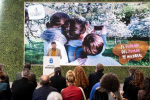 Persona realizando una presentación sobre la floración del manzana, con gran pantalla detrás de él y público