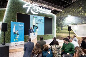 Persona realizando una presentación sobre el cartel del festiva de Nava, con gran pantalla detrás de él y público