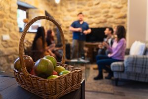 Foto manzanas en un cesto, al fondo personas sentadas y de pie en un alojamiento rural