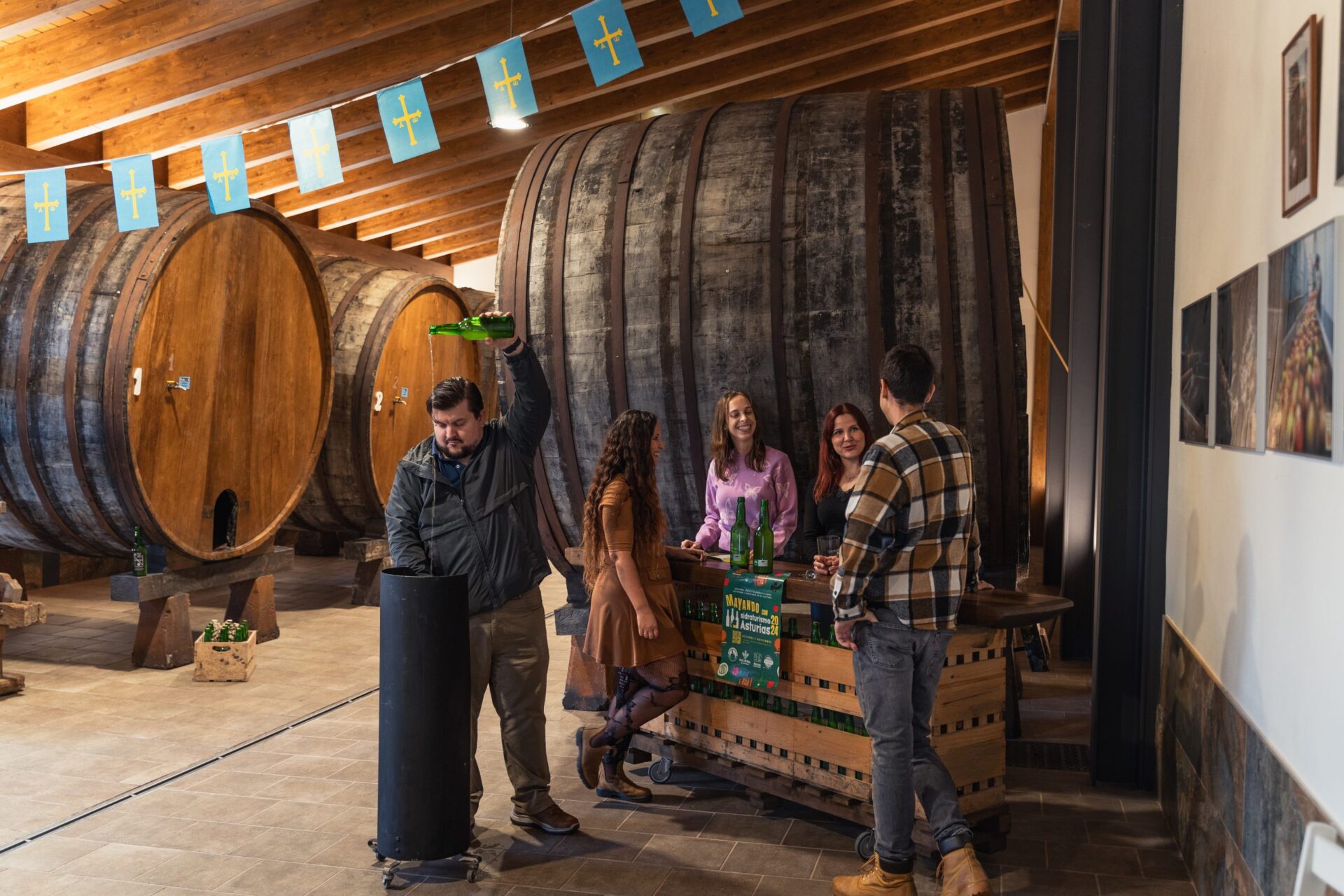 En un llagar de sidra asturiano, personas realizando una visita y una de ellas escanciando sidra
